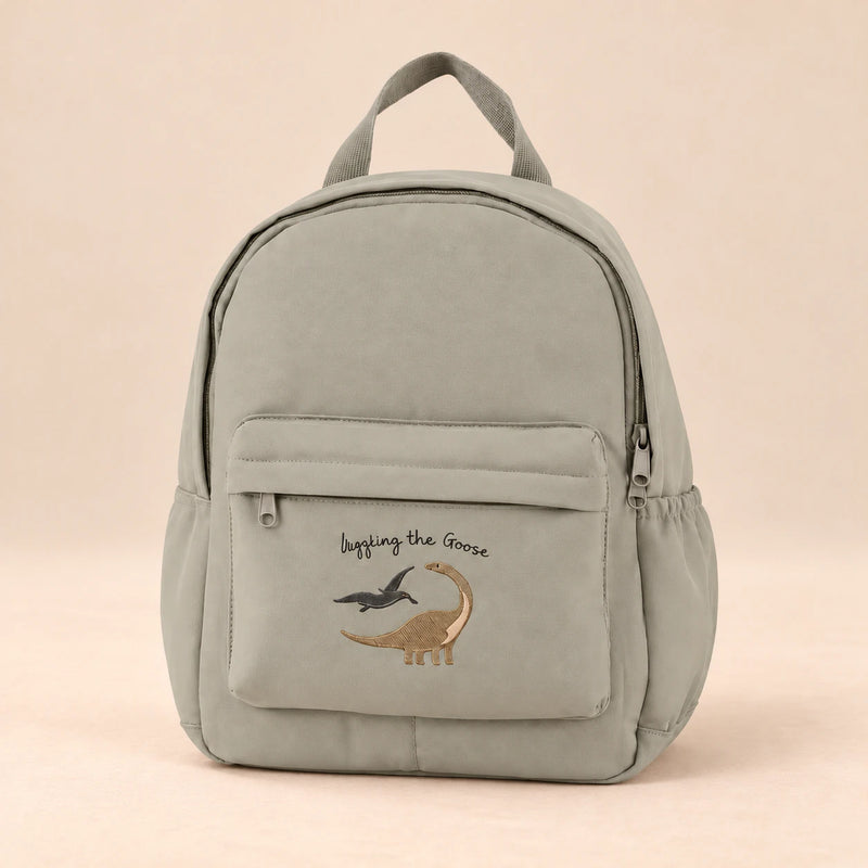 Little Explorer Large Backpack. Dino Soft Grey. Clean product photograph on a warm beige studio surface.