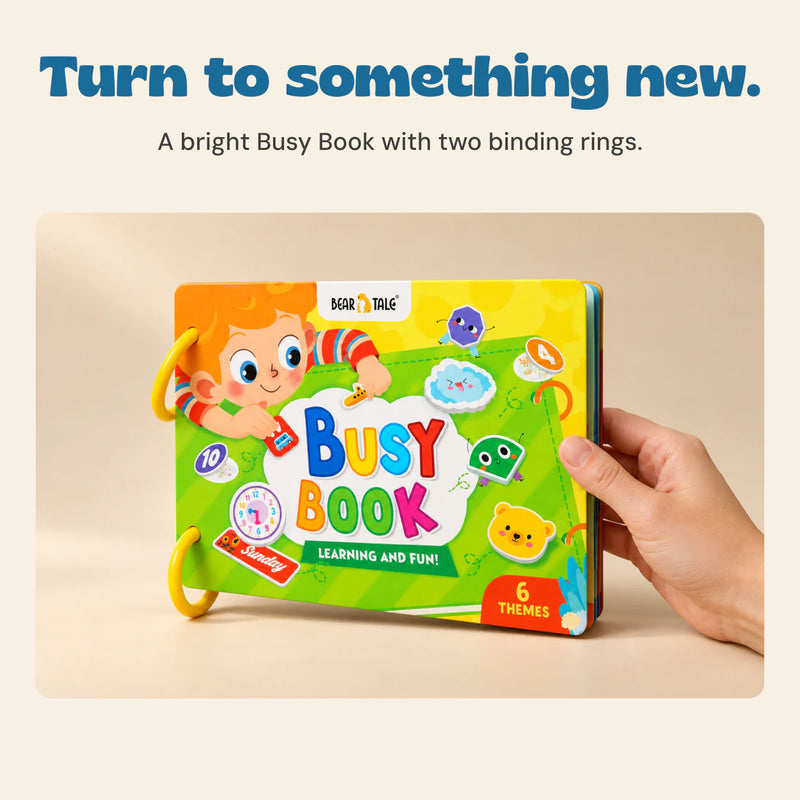 An adult hand holds the original green Busy Book with two yellow rings and its exact colourful cover artwork.