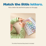 Child matching colourful alphabet pieces in the white preschool busy book at a wooden table.