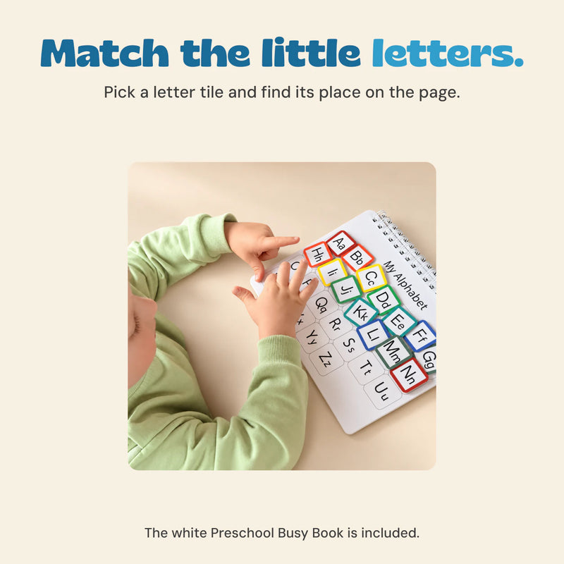 Child matching colourful alphabet pieces in the white preschool busy book at a wooden table.
