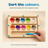 A hand guides a blue bead with the turquoise wand on the Ice Cream Sort maze board.