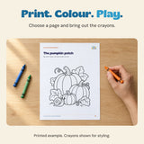 Adult hand holding an orange crayon beside the actual pumpkin patch colouring page printed on a loose sheet.