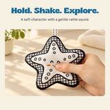 An adult hand holds the soft starfish rattle above a warm sunlit table.