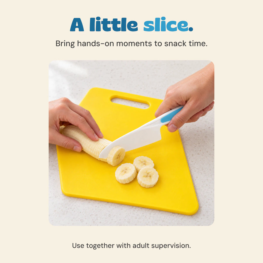 Adult hands demonstrate slicing a banana with the white and blue knife on the yellow cutting board.