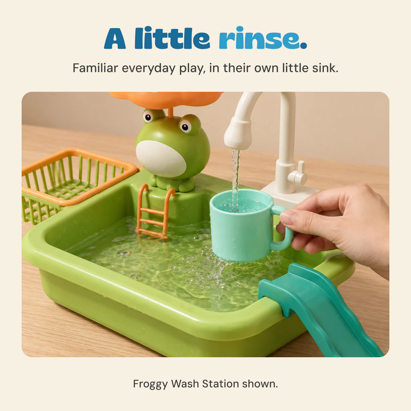 Adult hand holding a mint cup under the Froggy Wash Station tap, with the orange umbrella and turquoise slide visible.