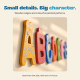 Close side view of wooden magnetic letters on a warm ivory surface, showing their thickness and painted details.