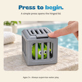 An adult fingertip presses the gray rescue cage lid tab, with one green puffer toy visible inside. Ages 3+. Adult supervision required for water play.