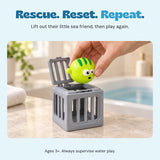 An adult hand lifts one green puffer toy from the open hinged top of its gray rescue cage. Ages 3+. Adult supervision required for water play.