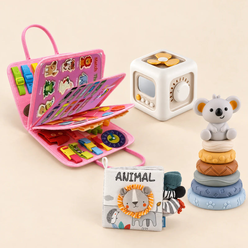 Mermaid Pink Plus busy board with an off-white and yellow activity cube, ANIMAL lion cloth book and six-ring koala stacking tower on a calm beige background.