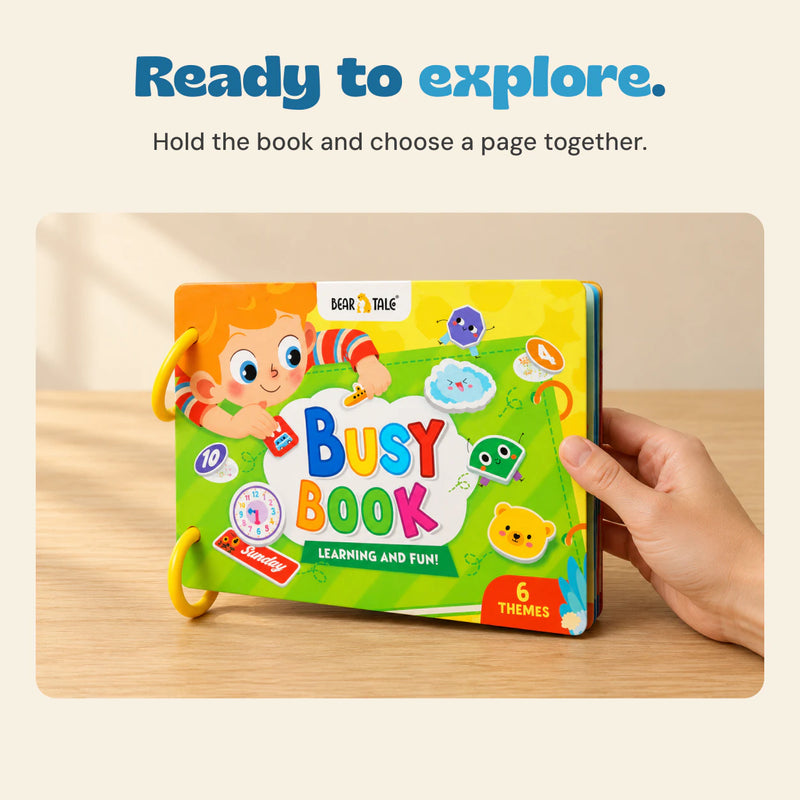 Adult hand holding the right cover edge of the green Busy Book, with both yellow rings and front artwork visible.