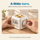 Adult hands hold the ivory busy cube and turn its side dial.