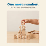 A hand places a wooden number three above a stack of natural wooden numbers.