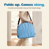 A cropped adult carries the folded blue tent by its black shoulder strap, with the top handle visible.