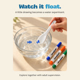 An adult hand dips the white ceramic spoon into water as a blue ink fish floats beside it.