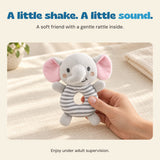 A hand holds the soft grey elephant rattle by its striped ring body.
