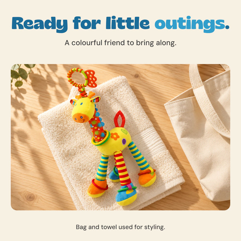 Yellow giraffe rattle resting on a cream towel beside a canvas bag on a wooden table.