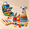 Ultimate Explorer Bundle with blue activity suitcase, five-ring koala stacker, two fabric animal toys, wooden activity board and colourful loose letters on a warm beige studio surface