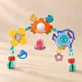 Ocean Friends stroller play arch with crab mirror, flower and hanging ocean toys on a warm beige studio surface.