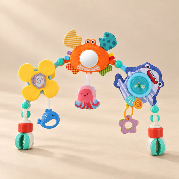 Ocean Friends stroller play arch with crab mirror, flower and hanging ocean toys on a warm beige studio surface.