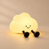 CloudGlow Tap Night Light glowing warm yellow with two black legs on a softly lit beige studio surface.