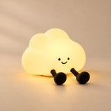 CloudGlow Tap Night Light glowing warm yellow with two black legs on a softly lit beige studio surface.