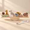 A wooden animal balance set on a straight plank and semicircular rocker, with a cotton threading cord in warm daylight.