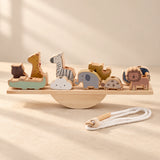 A wooden animal balance set on a straight plank and semicircular rocker, with a cotton threading cord in warm daylight.