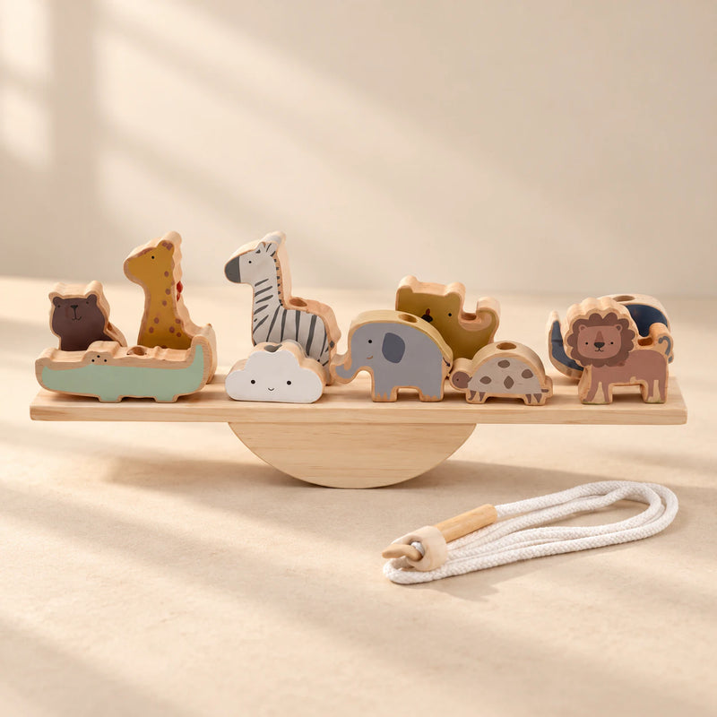 A wooden animal balance set on a straight plank and semicircular rocker, with a cotton threading cord in warm daylight.