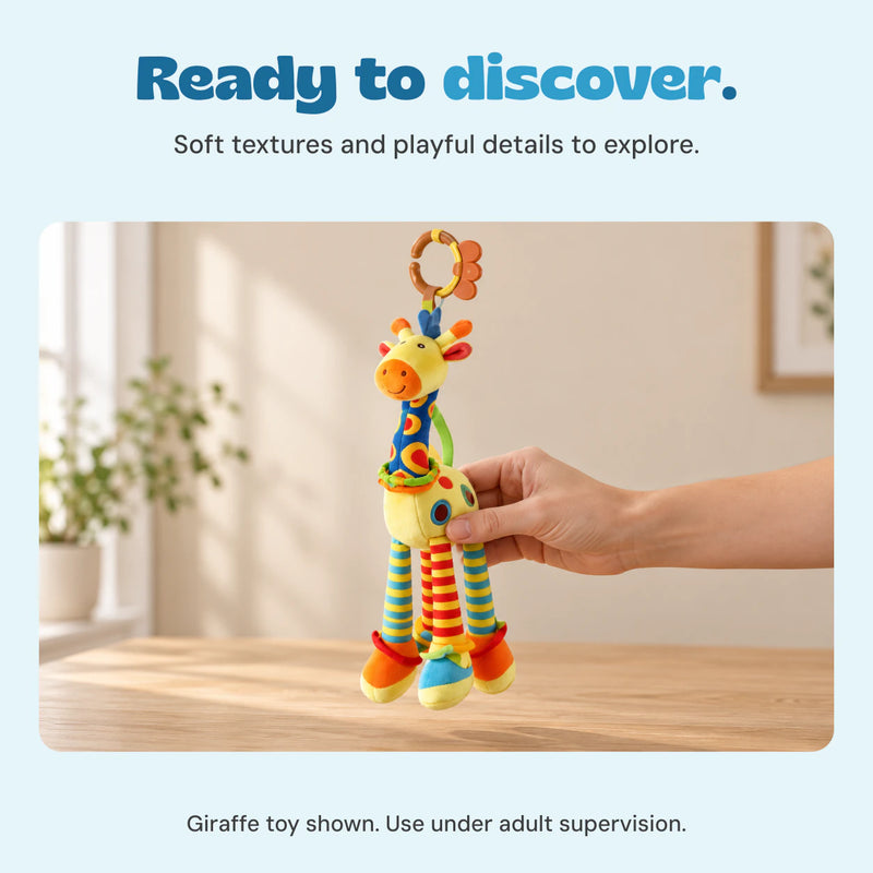 An adult hand holds the included giraffe toy above a wooden table in a warm naturally lit room.