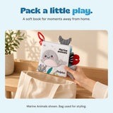 A hand holds the Marine Animals cloth book above a canvas bag. Bag used for styling.