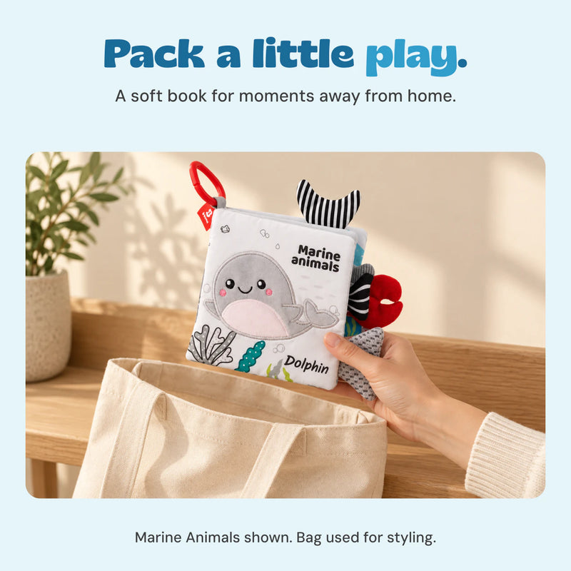 A hand holds the Marine Animals cloth book above a canvas bag. Bag used for styling.
