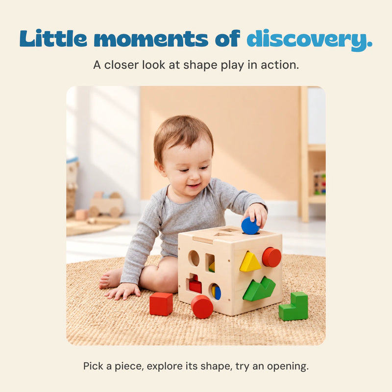 A child in a grey shirt holds a blue cylinder above the wooden sorting cube on a woven rug.