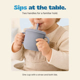 Existing photograph of a child holding the two handles of the silicone straw cup at the table.