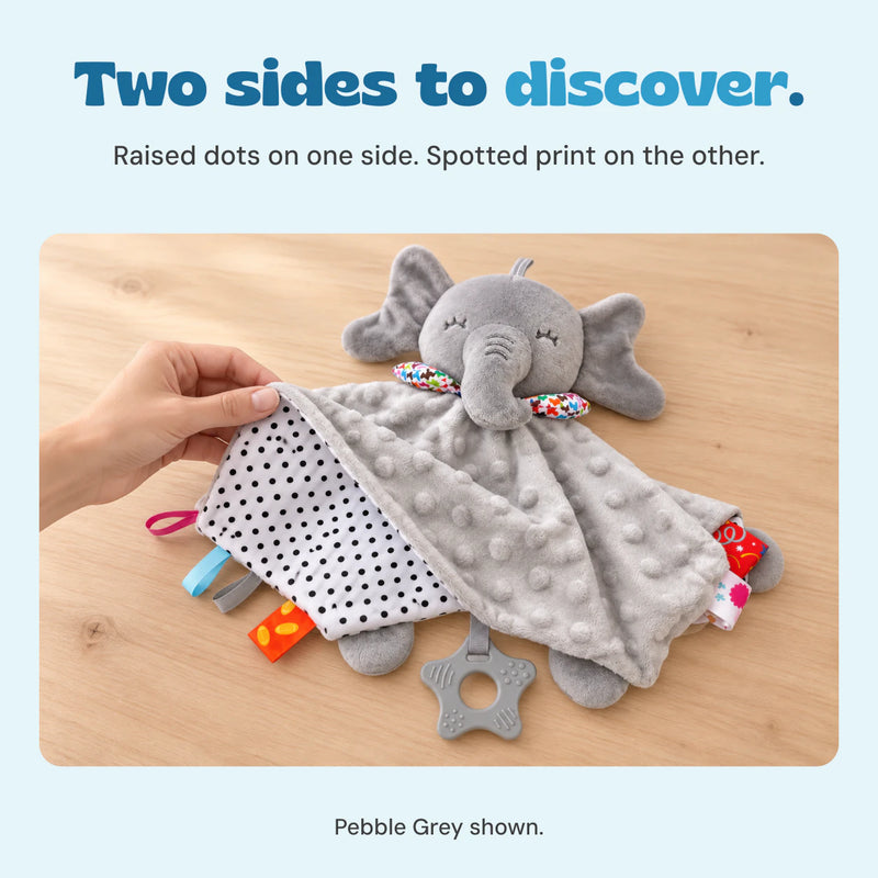 An adult hand lifts the grey elephant blanket edge to reveal its black-and-white spotted reverse.
