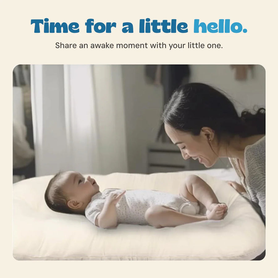 A parent shares a face-to-face moment with an awake baby in the cream lounger.