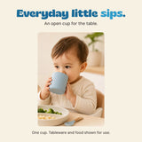 Original photograph of a child holding and drinking from the grey blue open cup at the table.