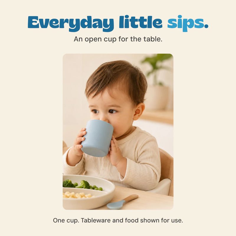 Original photograph of a child holding and drinking from the grey blue open cup at the table.