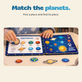 Hands match removable planet pieces to an open Space quiet book, with more planet pieces on the table.