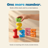 A hand balances a green four above a yellow two, red one and blue three, with pink six and orange five beside them.