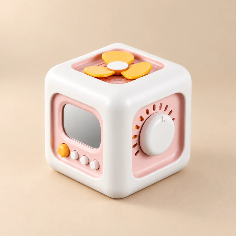 TibaToes Montessori Busy Cube in Pink/Yellow, showing its visible activity panels on a warm beige background.