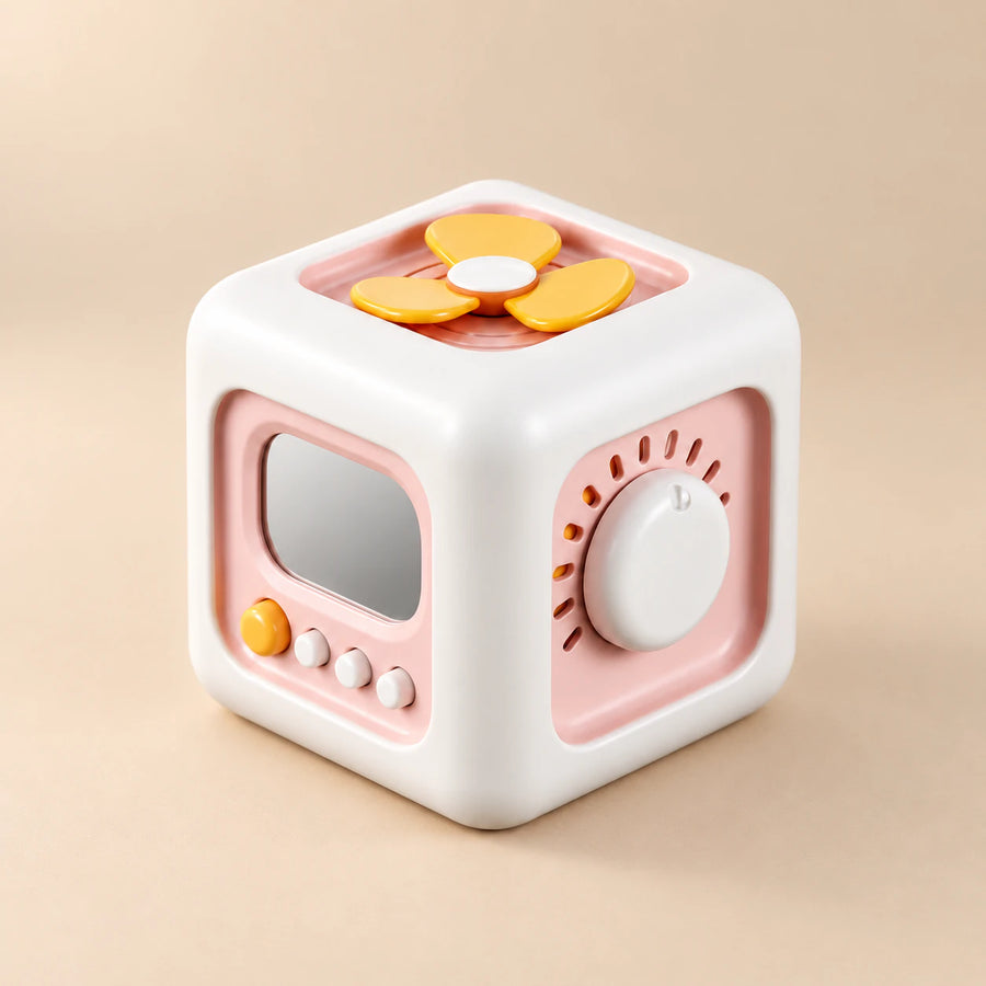 TibaToes Montessori Busy Cube in Pink/Yellow, showing its visible activity panels on a warm beige background.