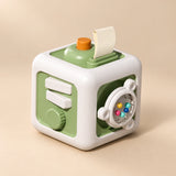 TibaToes Montessori Busy Cube in Green/White, showing its visible activity panels on a warm beige background.