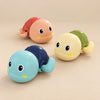 Three wind-up turtle bath toys in blue, peach and yellow on a smooth warm beige studio surface.
