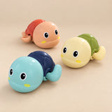 Three wind-up turtle bath toys in blue, peach and yellow on a smooth warm beige studio surface.