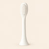 One ivory-white replacement brush attachment with an oval bristle head, slender stem and flared connector, shown alone on warm beige.