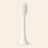 One ivory-white replacement brush attachment with an oval bristle head, slender stem and flared connector, shown alone on warm beige.