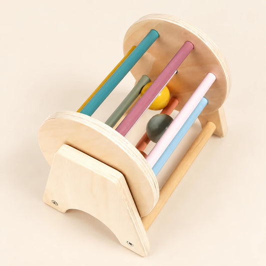 Wooden spinning drum with coloured bars and two balls in a natural wood stand on a pale beige background.