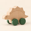 Stegosaur wooden rolling toy on a smooth pale warm beige background, showing its original shape and wheel design.