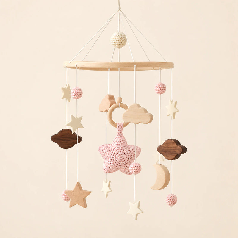 Pink hanging mobile with its source-matched wooden support, cords and individual charms on warm beige.
