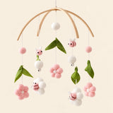 Pink Floral Bee hanging mobile with its source-matched wooden support, cords and individual charms on warm beige.